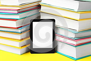 Modern e-book reader and stacks of hard cover books on yellow background, closeup