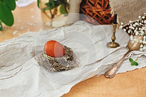 Modern Easter egg in nest on rustic table with spring flowers, candle,basket. Stylish red Easter egg painted in natural dye from