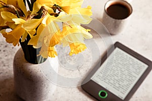 Modern ebook reader,  daffodils flowers on background. Top view, minimal flat lay style composition. Women desk, fashion blogger,