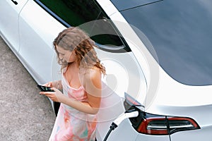 Modern eco woman recharge EV car with smartphone. Synchronos