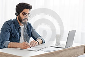 Modern education. Arab student guy learning online at home, looking at laptop computer, sitting at desk, free space