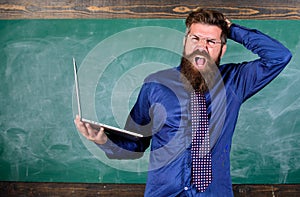 Modern educational program. Teacher bearded man with modern laptop chalkboard background. Hipster teacher surprised with