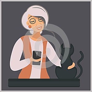 A modern elderly lady with a gadget stroking a black cat in the evening. Grandma and pet. Elegant woman with a cat