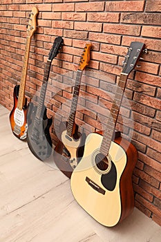 Modern electric and classical guitars near red brick wall indoors