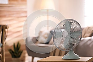 Modern electric fan on wooden table in living room. Space for text