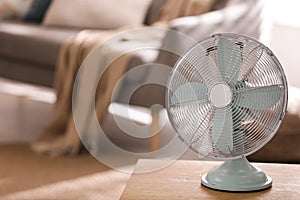 Modern electric fan on wooden table in living room. Space for text