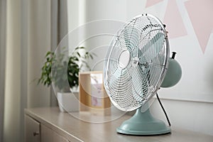 Modern electric fan on wooden table, space for text. Summer heat