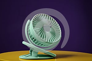 Modern electric fan on yellow table against violet background