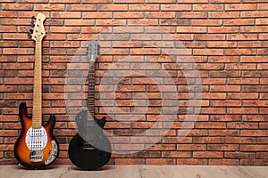 Modern electric guitars near red brick wall indoors. Space for text