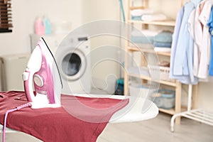 Modern electric iron and clean t-shirt on board in laundry room