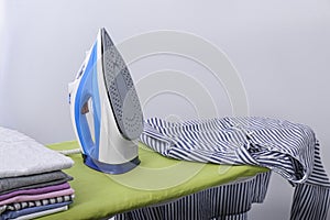 Modern electric iron and clothes on board indoors. Laundry day