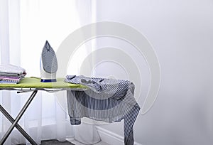 Modern electric iron and clothes on board  indoors. Laundry day