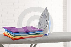 Modern electric iron and folded clothes on board