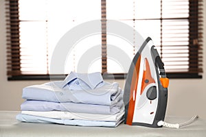 Modern electric iron and folded clothes on board