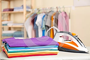 Modern electric iron and folded clothes on board indoors