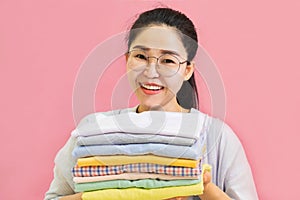 Modern Electric iron and stack of clothes on ironing board on pink background in laundry room. Household laundry ironing Woman