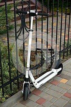 Modern electric kick scooter near metal fence outdoors