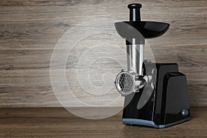 Modern electric meat grinder on wooden table. Space for text