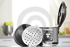 Modern electric multi cooker, parts and accessories on table in kitchen