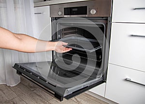 Modern electric oven with telescopic rails and steel baking tray. Hinged oven door. Black oven in a white kitchen. Automatic