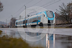 Modern electric passenger train during cold winter rain is rushing through city suburbs. Visible reflecions on the road