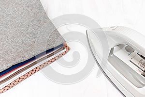 Modern electrical white iron near a stack of clothes close up - ironing, laundry and housework concept