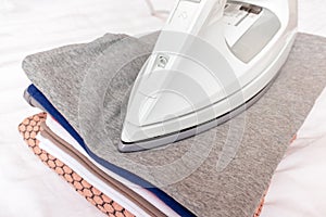 Modern electrical white iron on a stack of clothes close up - ironing, laundry and housework concept
