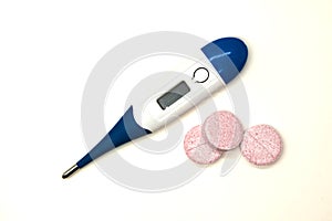 Modern electronic thermometer with pills closeup on white background