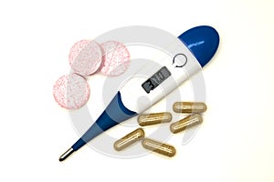 Modern electronic thermometer with pills closeup on white background