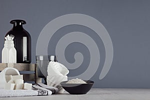 Modern elegant bathroom decor - cosmetics accessories in white ceramics bowls and dark glass vase on white wood board, grey wall.
