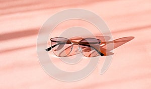 Modern elegant metal frame sunglasses on trendy pink paper background in sunlight. Flat lay. Tropical summer holidays