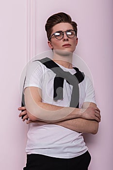 Modern elegant young hipster man with hairstyle with a trendy glasses in a white vintage t-shirt with a black cardigan posing near