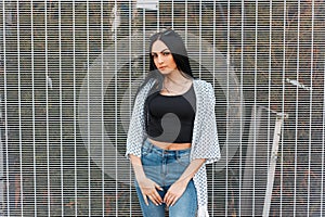 Modern elegant young hipster woman with long gorgeous hair in a black fashionable t-shirt in a summer vintage jacket in jeans