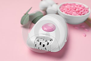 Modern epilator with depilatory wax on pink background, closeup