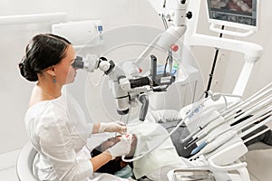 Modern equipment microscope in dental office. Young woman dentist treating root canals. Man patient lying on dentist