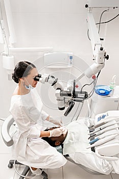 Modern equipment microscope in dental office. Young woman dentist treating root canals. Man patient lying on dentist