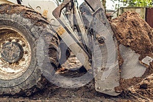 The modern excavator performs excavation work on the construction site. View on the big dirty wheel of backhoe and on