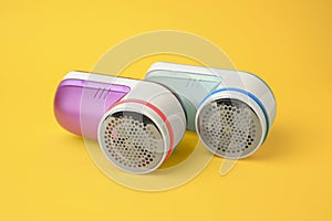 Modern fabric shavers in different colors on yellow background, closeup