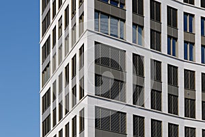 Modern facade with typical rectangular windows, reflection glass and randomly louvers against blue sky.