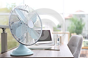 Modern fan on wooden table in office, space for text. Summer heat