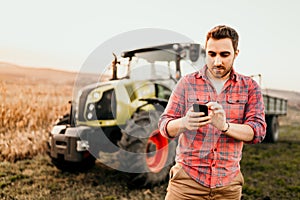 Modern farmer working and harvesting using smartphone in modern agriculture with tractor background