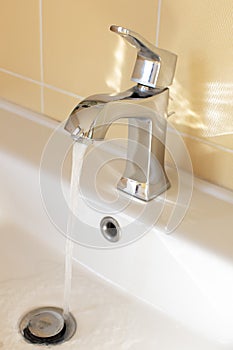 Modern faucet in yellow bathroom with running water, close up, side view. Concept hygiene, house cleaning, water saving, supply