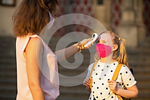 Modern female teacher and pupil measures temperature outdoors