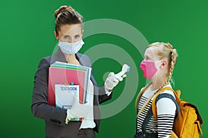 Modern female teacher and school girl measures temperature