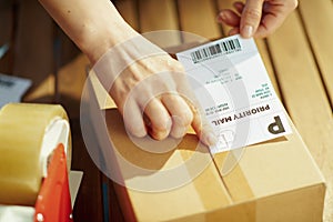 Modern female in warehouse applying shipping label to parcel