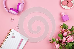 Modern female working space, top view. Women`s or girls things, wireless headphones, roses, perfume, stationery on pink backround