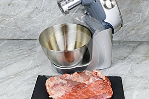 Modern food processor with meat grinder and peace of pork meat on a kitchen table