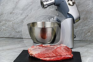 Modern food processor with meat grinder and peace of pork meat on a kitchen table