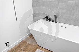 A modern, free standing wall mounted bathtub with a black matt tap, standing in a bathroom lined with ceramic tiles.