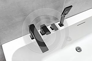A modern, free standing wall mounted bathtub with a black matt tap, standing in a bathroom lined with ceramic tiles.